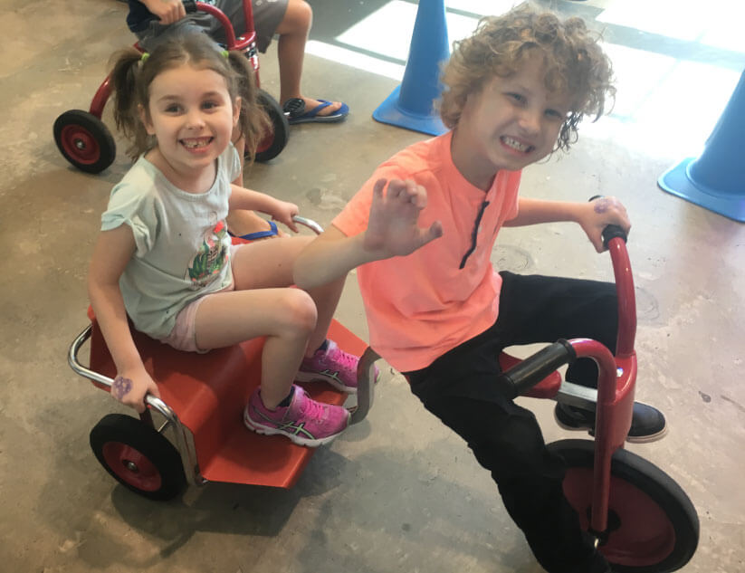 Ricky and Olivia sit on a red tricycle while playing at Children's museum of Phoenix
